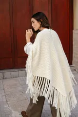 Poncho triangular de lana en color crudo, con diseño de tejido texturizado y terminaciones de flecos largos en todo el borde.