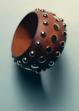 Pulsera rígida de madera marrón con tachas metálicas doradas distribuidas en su superficie.