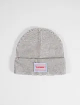 Gorro tejido tipo beanie en color gris, con diseño acanalado y vuelta en el borde. Presenta un parche rectangular frontal con estampado de rombos y el logo de la marca en color rojo.