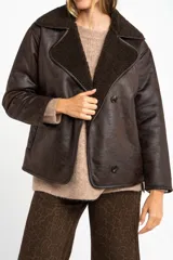 Chaqueta tipo gamulán de calce oversize en color marrón oscuro, con exterior de poliéster y forro de corderito sintético. Presenta cuello de solapa ancha y cierre frontal con botones.