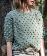 Sweater marrón de manga corta confeccionado en 100% lana merino con textura de bodoques tridimensionales en relieve y cuello redondo a la base.