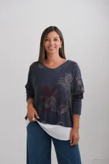 Sweter de corte amplio con diseño de doble capa, que presenta una capa superior estampada con motivos florales en tonos azules y una capa inferior blanca visible en el ruedo. Posee escote en V y mangas largas.