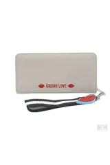 Billetera rectangular de cuero sintético color beige con parche frontal blanco que incluye el texto 'MON AMOUR' y logo de la marca. Cuenta con cierre perimetral y una correa de muñeca desmontable con un dije de labios rojos.