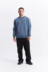 Buzo de cuello redondo en color azul, con diseño de calce regular. Presenta bolsillos laterales integrados, puños y ruedo acanalados, y un pequeño estampado gráfico en el pecho. Incluye un detalle de etiqueta en la manga derecha.