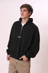 Sudadera negra con cierre de cremallera metálica en el cuello y estampado con texto en el pecho.
