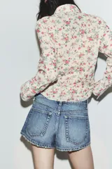 Camisa entallada de manga larga con cuello solapa, cierre frontal de botones y detalle de volantes en el delantero, confeccionada en tejido con estampado floral.
