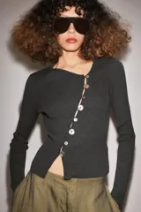 Chaqueta de punto color gris oscuro, con escote en pico y manga larga. Presenta cierre frontal con botones nacarados dispuestos de manera asimétrica.