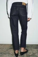 Jeans de tiro medio con corte slim leg, confeccionados en denim color beige. Presentan cintura con trabillas, diseño clásico de cinco bolsillos y cierre frontal con cremallera y botón metálico.