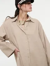 Vestido camisero oversized color beige, confeccionado en 83% ramié y 17% algodón, con mangas amplias, puños altos y cartera con botones delanteros.