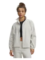 Campera Under Armour Unstoppable Wvn Fz de color gris claro, confeccionada en tejido técnico con tecnología UA Storm que repele el agua. Presenta cuello alto, cierre frontal completo, hombros caídos, bolsillos laterales con cierre y puños y bajo elásticos con cordón ajustable.
