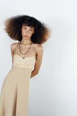 Vestido midi de color beige con escote recto adornado con un panel de encaje semitransparente, tirantes finos ajustables y falda fluida con cierre lateral con cremallera oculta.