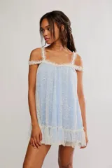 Vestido corto de tul celeste con capa superior de encaje floral blanco, escote recto, tirantes finos con volados, mangas caídas sobre los hombros y volado inferior.