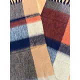 Bufanda rectangular de tejido grueso con diseño de cuadros en tonos azul, naranja, gris y beige, terminada con flecos en los extremos.