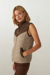 Chaleco de lana fina sin teñir con diseño acolchado en rombos y canesú en contraste. Cuenta con cuello alto, cierre frontal de cremallera y bolsillos laterales.