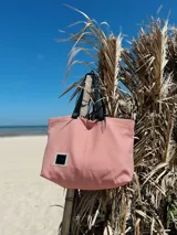 Bolso tipo tote rayado en tonos rosa y blanco, con asas cortas negras y correa larga regulable negra.