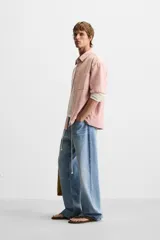 Camisa de corte relajado confeccionada en algodón, con estampado de cuadros pequeños en tonos rosados. Presenta cuello solapa, manga corta y bolsillo plastrón en el pecho con cierre frontal de botones.