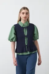 Chaleco tejido de punto color azul marino, con trama texturada y cierre frontal mediante lazos. Posee cuello a la base y terminación con volado en el ruedo.