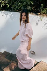 Camisa amplia de color rosado, con diseño estilo capa, cuello redondo y manga corta amplia. Cuenta con un bajo ajustable mediante lazada lateral.