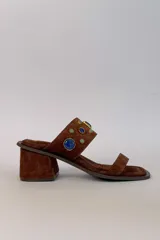 Sandalia de tacón ancho color marrón, confeccionada en gamuza, con puntera cuadrada, tira delantera fina y tira ancha superior decorada con apliques de piedras en tonos azules y bordes dorados.