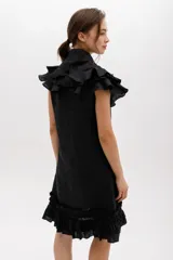 Vestido corto de lino color negro, con silueta recta y largo por encima de la rodilla. Incluye un cuello removible con volados y lazo, y detalles de volados en las sisas y el ruedo.