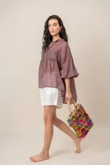 Blusa color malva con volados en el cuello y mangas largas abullonadas, de corte amplio y ligero.