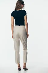 Pantalón de tiro alto color beige, con detalle de costuras marcadas en el delantero y la espalda. Incluye bolsillos delanteros de vivo y cierre frontal con cremallera, botón interior y gancho metálico.