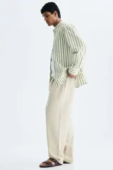 Camisa de popelina de algodón con cuello inglés, tapeta clásica, bolsillo superior abierto y canesú con pliegue en la espalda. Cuenta con mangas largas, puños ajustables con botón y bajo ligeramente redondeado. Presenta un diseño de rayas verticales en tonos verde y blanco.