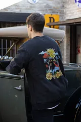 Buzo negro con efecto lavado y estampado en la espalda de un sol, hongos y flores.