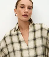 Blusa de viscosa con estampado de cuadros en tonos beige y verde. Presenta cuello en V, cierre frontal con botones y mangas 3/4 abullonadas con puños elásticos.