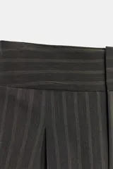 Pantalón balloon de tiro alto y diseño abuchonado, en color marrón oscuro con sutiles rayas verticales. Cuenta con pinzas y pliegues pronunciados en el delantero.