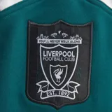 Buzo deportivo adidas del Liverpool F.C., modelo Crew Sweat 95, en color verde, negro y blanco. Presenta diseño retro con bloques de color, cuello redondo, el logo de adidas, el escudo del club en el centro y patrocinador Carlsberg estampado en el frente.