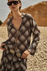 Camisa de manga larga con estampado escocés en tonos chocolate, blanco y gris. Presenta cuello camisero, cierre frontal con lazos y puños con lazos ajustables.