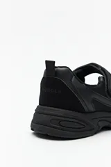 Zapatillas deportivas negras con suela blanca de 4cm de alto y tira ajustable con velcro.