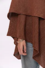 Ruana tejida de punto con cuello alto, confeccionada en una mezcla de algodón y lurex que le otorga un acabado brillante. Presenta un diseño asimétrico con caída fluida y holgada.