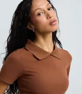 Blusa polo beige de manga corta, confeccionada en tejido canelado de rib de algodón con elastano, que proporciona un ajuste cómodo y una caída ajustada.