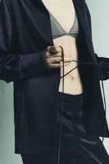 Camisa de manga larga color azul marino, confeccionada en tejido satinado. Presenta cuello solapa, puños anchos y cierre frontal mediante lazada ajustable en el centro.