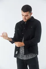 Sobrecamisa de jean color tostado, con cuello clásico, cierre frontal con botones y dos bolsillos frontales con solapa. Presenta mangas largas con puños abotonados y un pequeño parche decorativo en el ruedo.