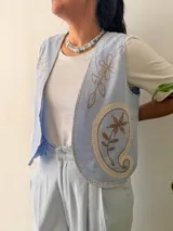 Chaleco celeste con delicados bordados florales en tonos beige, sin mangas y con escote en V.
