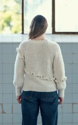 Sweater tejido a crochet en lana merino color crudo, con cuello redondo y manga larga. Presenta una trenza diagonal con volados en el frente.