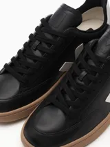 Zapatillas Veja V-12 de cuero negro con logo lateral en forma de V color blanco y contrafuerte blanco. Suela de goma color caramelo.