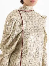 Top de seda con estampado floral pequeño, cuello alto con lazo integrado, mangas largas abullonadas con frunces en los hombros y puños camiseros con botones. Presenta detalles de ribete en color contrastante.