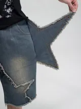 Bermuda de jean con diseño deconstruido y paneles superpuestos con bordes deshilachados. Presenta un efecto de lavado desgastado, cierre frontal y botones metálicos.