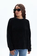Sweater de tejido chenille en color negro, con cuello redondo, mangas largas y puños acanalados. Presenta una textura suave y un corte holgado.