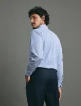 Camisa de vestir de manga larga con diseño de rayas verticales finas en color celeste y blanco. Presenta cuello clásico, cierre frontal con botones y un bolsillo en el pecho.