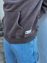 Buzo canguro marrón con capucha y cordones, de corte amplio y estilo urbano.