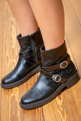 Bota corta de cuero charolado color bordó, con suela plana de goma negra, cierre lateral y tiras decorativas con hebillas metálicas en el tobillo.