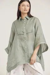 Camisa de manga ancha, color verde salvia, con cuello camisero y cierre frontal de botones. Presenta detalles de pespunte decorativo en el canesú frontal.