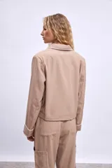 Cazadora color beige con bordados en hilo blanco en cuello, bolsillos y puños.