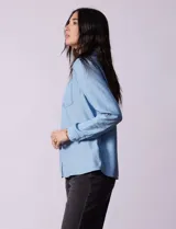 Camisa celeste de lyocell, con cuello a la base, escote en V y abertura central con botones. Tiene bolsillos aplicados en la parte delantera y mangas 3/4 regulables con presilla y botón.