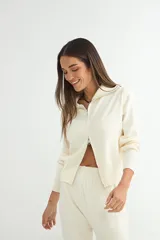 Conjunto de dos piezas tejido en color crema, compuesto por un cárdigan con cierre frontal completo y cuello alto, y pantalón de corte recto con cintura elástica.